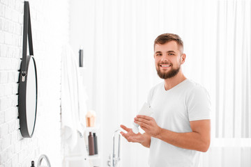 Naklejka na ściany i meble Handsome young man with tube of cream in bathroom