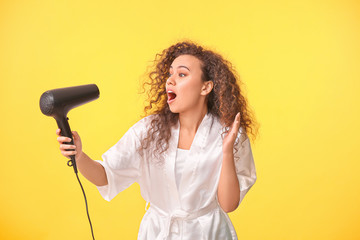 Beautiful surprised African-American woman with blow dryer on color background