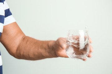 Senior man with Parkinson syndrome holding glass of water on grey background