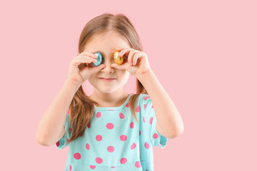 Cute little girl with sweet chocolate eggs on color background