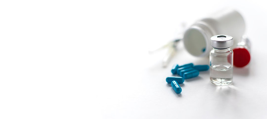 Long wide medical banner with vials with vaccine, big blue pills and plastic syringes on white background, selected focus. Vaccination and health care concept. Infection prevention banner.