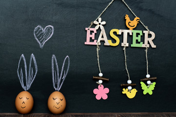 wooden inscription Happy Easter on a black slate. two chicken eggs below with chalked ears. place for text. mocap
