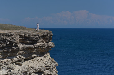 a girl in white clothes stands on the edge of a cliff above the sea