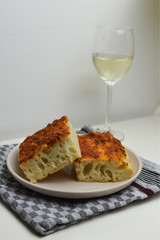 Traditional italian bread, focaccia siciliana with sardines, tomatoes and oregano, glass of white wine in the background