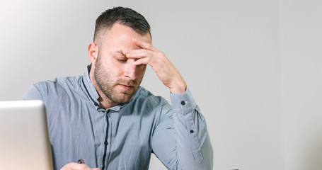 Frustrated businessman under stress nervously filling 1040 tax form with calculator at office desk.