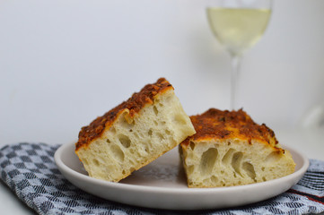 Traditional italian bread, focaccia siciliana with sardines, tomatoes and oregano, glass of white wine in the background