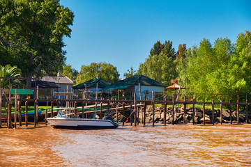 Tigra delta in Argentina, river system of the Parana Delta North from capital Buenos Aires. Lush vegetation, wooden houses. Motor boat by pier. Orange clay water of Lujan River delta system