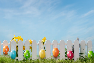 Spring grass and wooden fence with easter eggs and flower on cloudy sky