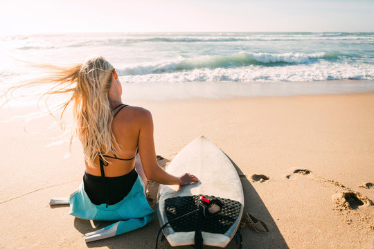 Woman sitting next to surfboard on beach