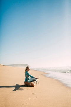 Woman kneeling holding surfboard on beach