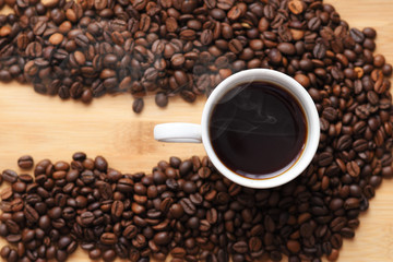 white Cup with hot coffee surrounded by coffee beans on wooden surface. with place under the inscription