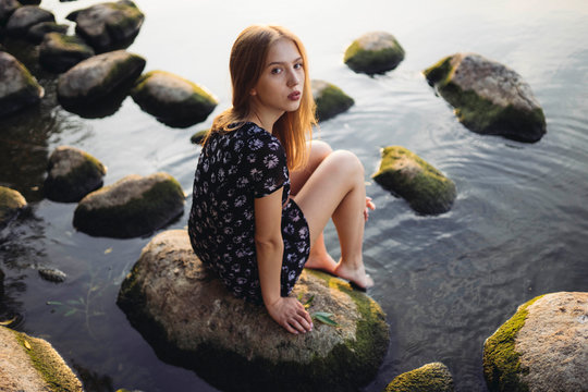 Woman wearing black dress sitting on rock in sea