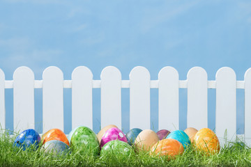 Spring grass and wooden fence with easter eggs on cloudy sky