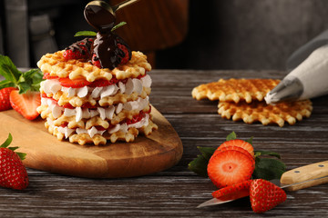 A multilayer waffle cake with ripe strawberries and whipped cream, decorated with mint and...