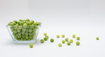 Chicharos  pelados en un recipiente de cristal con unos chicharos con cascara a un costado sobre un fondo blanco