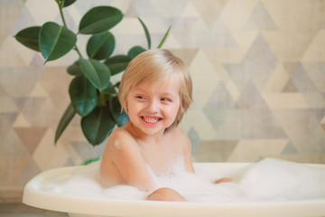 Obraz na płótnie Canvas Children's hygiene. The child bathes in a large bath. Happy cute boy 4-5 years old with foam in his hair.