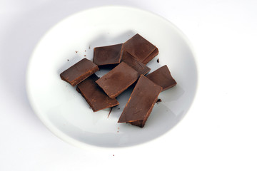 Pieces of dark chocolate on a white saucer isolate on a white background close-up.