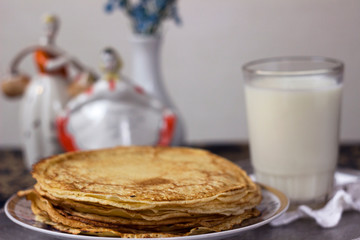 Traditional flat pancakes on a buttercup with milk, vintage ceramic figurines in the background. Slavic traditions, Shrovetide