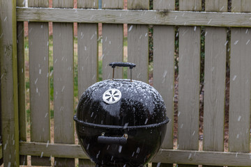 Snow covered grill in a backyard beside a wooden fence.