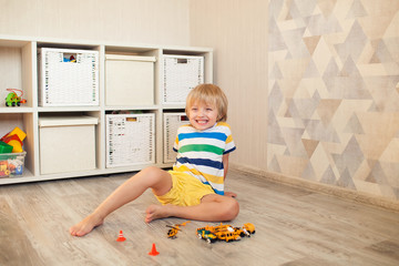 Happy cute boy blond 4-5 years old playing in the nursery with cars on the floor. Bright clothes, game, development.