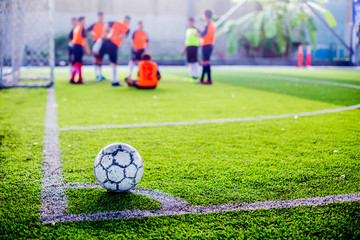 soccer ball on green artificial turf at corner of football field with blurry players background, football on corner for corner kick with blurry kid soccer players, soccer training or football match.