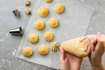 Cooking profiteroles, female hands  squeeze  the dough from the bag onto parchment, for baking.