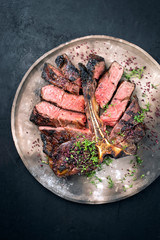 Barbecue dry aged wagyu porterhouse beef steak sliced with large fillet piece with herbs and red salt as top view on a modern design rustic plate with copy space