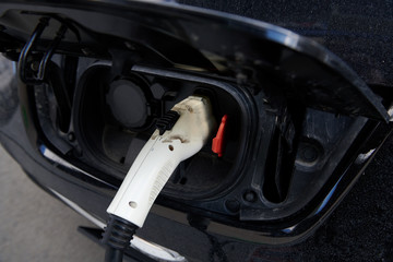 White plastic plug-in connector in the electric car. Car while charging battery. Ecological transportation. Closeup.