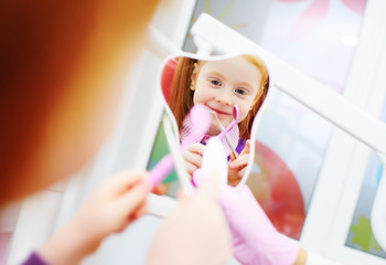 child-a little red-haired girl smiling looking in the mirror sitting in the dental chair.