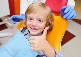 smiling baby boy with blond curly hair in dental chair.