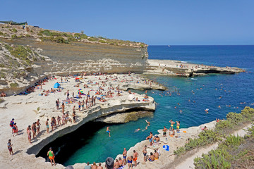 Crowds gather to swim in the naturally formed St. Peter’s Pool near Marsaxlokk on the island of Malta. - obrazy, fototapety, plakaty