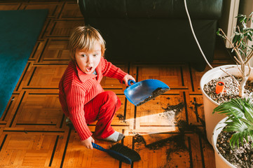 Very messy baby with funny facial expression cleaning plant soil from the floor