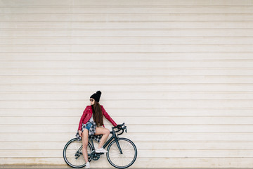 Brunette girl with very long hair and dressed in red leather jacket, waiting sitting on her urban bike