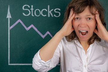 The concept of a business crisis, a young businesswoman clutching her head in horror, in the background is a stock chart with a negative trend.