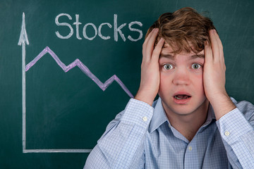 Concept business crisis, angry young businessman in horror clutching his head, in the background is...