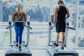 Sport, fitness, lifestyle, technology and people concept - close up of woman and men legs walking on treadmills in the gym.