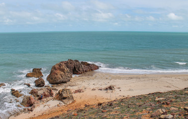 Panoramic view of Pedra Furada, a famous tourist attraction in Jericoacoara, Ceará, with the arch-shaped rock and beach in the foreground and turquoise blue waters under a sunny sky