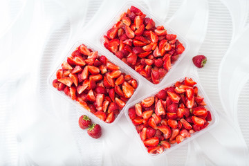 Sliced pieces of strawberries in transparent containers on a white background, top view