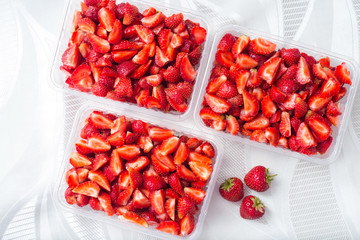 Sliced pieces of strawberries in transparent containers on a white background, top view