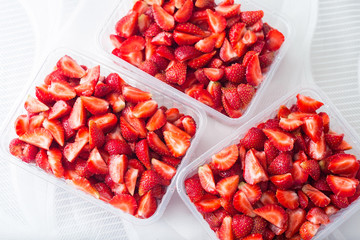 Sliced pieces of strawberries in transparent containers on a white background, top view