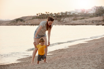 Happy mother and toddler play on the seaside. Mom and baby play in the sea beach. Mother's love. Lifestyle. Summer rest. Family vacation. Mothers day.