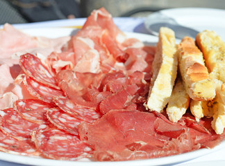 Plate with salami, ham and different sorts of cold cuts with toasted Italian bread and dried herbs. Selective focus