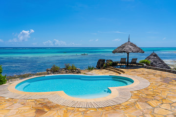 Swimming pool and straw umbrella on a tropical beach near the sea in sunny day on the island of Zanzibar, Tanzania, Africa