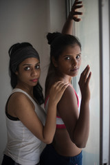 A beautiful and young Indian Bengali lesbian couple in sports inner/underwear are interacting in a intimate way in front of a glass window in white background. Dark and fare model, Indian lifestyle