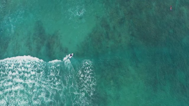 Drone videography of a surfer gliding the waves in Hawaii as the sun shines high in the sky. The perfect summertime activity.