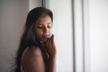 Portrait of an attractive young brunette dark skinned Indian Bengali girl in western sportswear in front a glass window in white studio background. Indian lifestyle