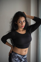 Portrait of an attractive young brunette Indian Bengali girl in western sportswear in front a glass window in white studio background. Indian lifestyle