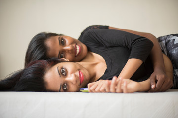 Obraz premium Two black and white attractive young brunette Indian Bengali women in black western dress are sleeping together in white bed in white studio background. Indian lifestyle.