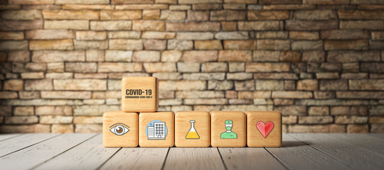 cubes with text COVID-19 and health icons in front of a brick wall on wooden floor