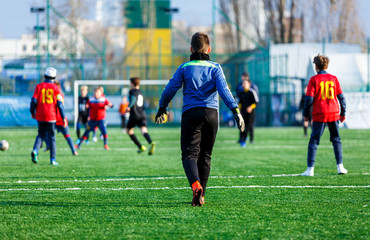 Obraz na płótnie Canvas Boys in red and black sportswear plays football on field, dribbles ball. Young soccer players with ball on green grass. Training, football, active lifestyle for kids concept